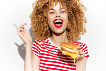 Cheerful woman with curly hair holding a burger, expressing joy and excitement, on a bright white background Perfect for healthy eating concepts