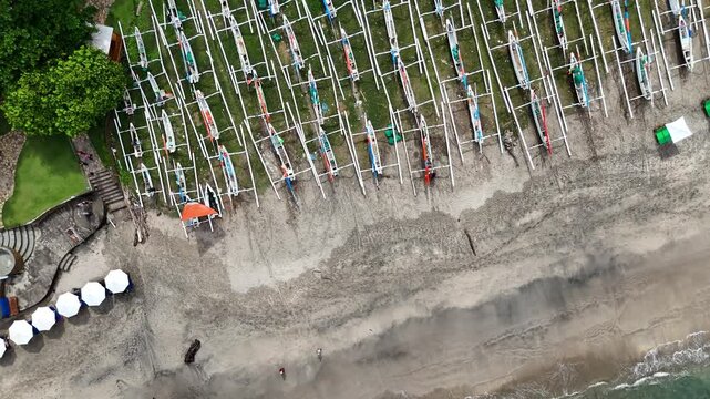 Aerial view drone footge rocet mode real time  of traditional fishing boats lined up on a tropical beach with turquoise waves and palm trees in Bali, Indonesia.
