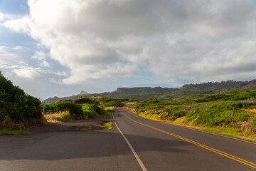 A winding road cuts through lush green hills under a cloudy sky.