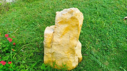 A pale yellow garden stone placed on a green grassy lawn, adding a natural decorative element to...
