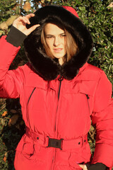 Portrait of beautiful young woman in red winter jacket with black details by natural sunset warm colour sunlight. Fashion model with natural make up and hair in puffer jacket, winter clothing 