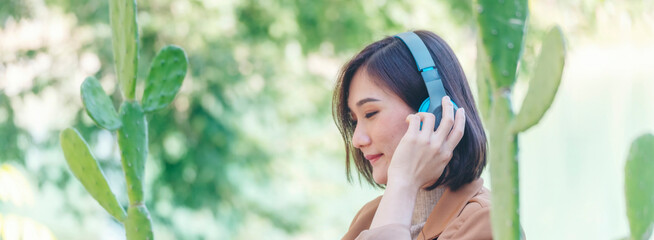 Banner Happy asian woman use headphones listen to music from smartphone outdoor in green park....