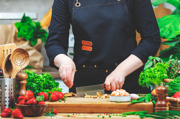 Chef cooking food in the kitchen. Cook cuts walnuts, prepare gourmet salad. Wooden table,...