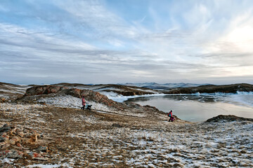 Girl with stroller walks through snowy landscape on Lake Baikal Small Sea at sunset