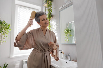 Elderly European woman pensioner middle age smiles and combs her gray hair with wooden comb.