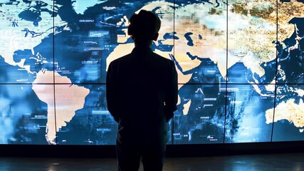 Silhouette of a person observing a digital world map on a large screen in a modern tech environment - Powered by Adobe