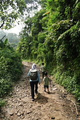 A muslim woman and her two children are walking down a muddy path in a forest