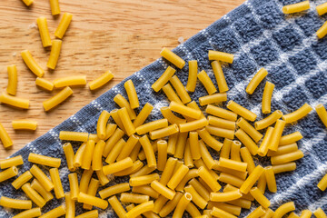 Close up shot of elbow macaroni scattered in a wooden table, background and texture