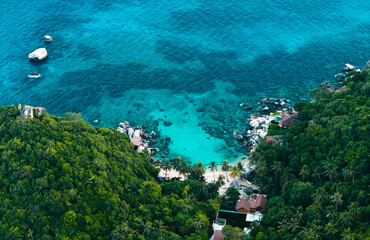 aerial view reveals a stunning, secluded tropical bay, nestled amidst lush green hills. The vibrant...