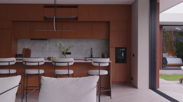 Stylish open-concept kitchen showcases elegant wooden cabinetry, minimalistic bar stools, and natural light streaming through large windows.