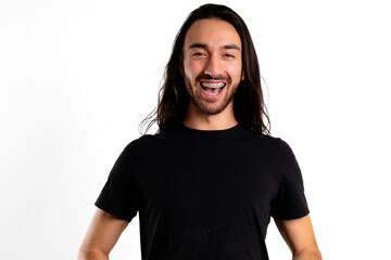 Smiling happily with braces and open mouth, young Latin man looks at camera against white background