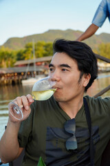 Young Asian man drinking white wine in a boat on a lake in the evening.