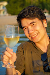 Young Asian man drinking white wine in a boat on a lake in the evening.