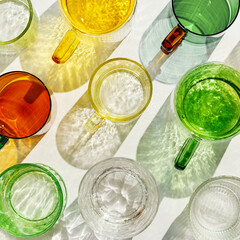 Colorful glowing glass cups on white background, casting artistic light reflections and shadows in natural sunlight. Summer drink concept, minimal trend pattern of transparent glasses, caustics