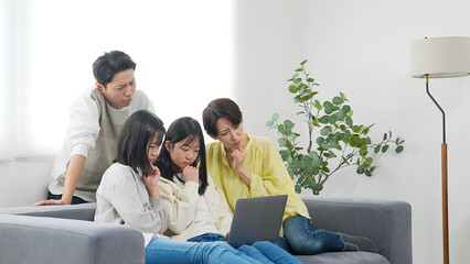 ノートパソコンを見ながら悩む小学生姉妹と家族