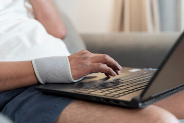 Close-up of injured man's hand wearing wrist support while typing on laptop computer during recovery at home