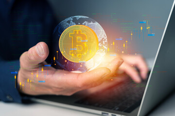 Hand holding glowing bitcoin symbol with global network and stock market candlestick chart on laptop screen
