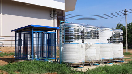 Metal water tank. Four stainless steel water tanks with water pump in blue cage installed on the side of a gymnasium or industrial plant with copy space. selective focus