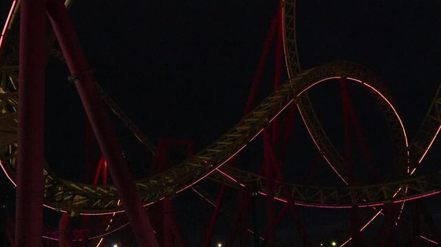 Rollercoaster Night Ride Amusement Park: Thrilling nighttime rollercoaster ride at an amusement park, showcasing dynamic curves and red lighting effects.