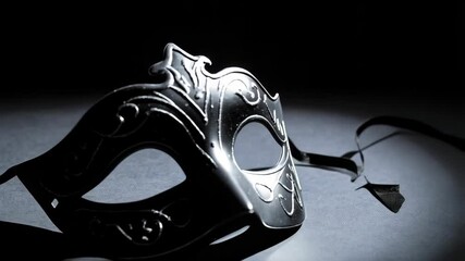 Elegant black masquerade mask with ornate filigree resting on a dimly lit surface with ribbon ties, creating a mysterious atmosphere. - Powered by Adobe