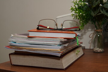 Scholarly Still Life: Eyeglasses Resting Atop a Tower of Books and Papers on a Wooden Desk