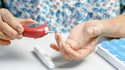 Elderly person using blood glucose meter to check sugar level, diabetes management at home, close...