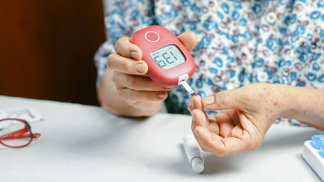 Elderly person checking blood sugar level with glucose meter, hand holding device and test strip, diabetes management at home, health care concept
