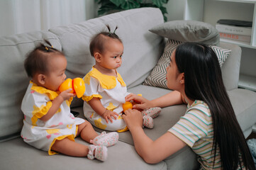 Portrait of Single mother spends happy time with her twin daughters in a warm room at home. Take care of baby with love and care.