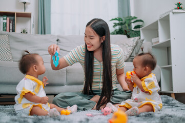 Portrait of Young Asian mother shares a happy moment with her twin daughters while sitting on a soft carpet in a cozy room at home. Leisure activities with family