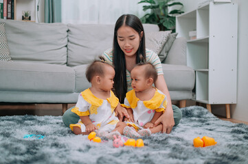 Portrait of Young Asian mother shares a happy moment with her twin daughters while sitting on a soft carpet in a cozy room at home. Leisure activities with family