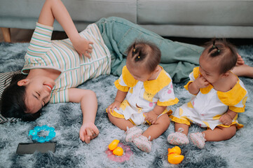 High angle view shot, Young mother lies on a carpet taking care of her twins while they play with toys in the living room at home.