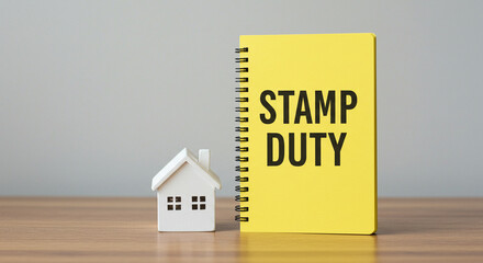 A small white house model next to a yellow notepad with the words stamp duty written on it in black ink