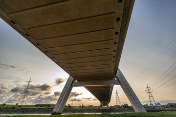 View from beneath the Flintshire Bridge at sunrise, highlighting its concrete underside and supporting structures, with power lines and pylons visible against the sky