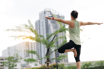 Asian woman fitness yoga workout. Stretching exercise reduces medical injury risk, shoulder pain, muscle strain and inflammation. Focused wellness and healthcare in an urban city at sunset