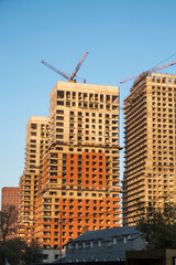 High-rise buildings under construction with tower cranes silhouetted against a clear sunrise sky....