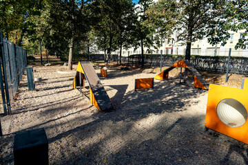 Outdoor dog playground featuring agility equipment in a fenced park area surrounded by trees....