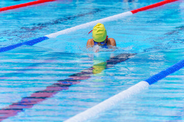 Swimmer child swims breaststroke swimming style in a race swimming pool. Water sports and competition, learning to swim classes for children.