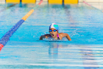 Swimmer child swims butterfly swimming style in a race swimming pool. Water sports and competition, learning to swim classes for children.