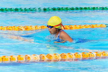 Swimmer child swims breaststroke swimming style in a race swimming pool. Water sports and competition, learning to swim classes for children.