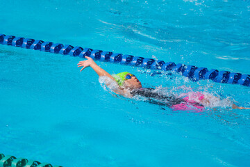 Swimmer child swims backstroke swimming style in a race swimming pool. Water sports and competition, learning to swim classes for children.