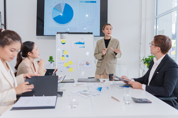 Group of Asian business people present their work on a table with graph paper.