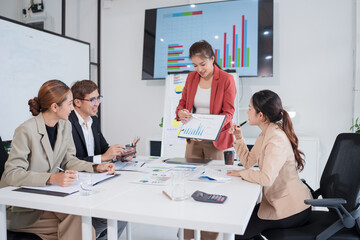 Group of Asian businesspeople sit at a table with graph paper in a meeting.