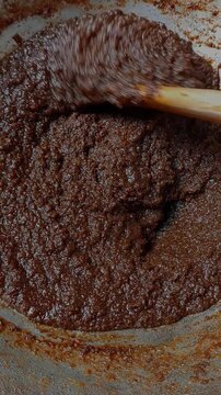 Preparing shito in a big metal pan. Final stage of preparing brown stew, stirring with wooden spatula, after adding fish powder to make shito, a Ghanaian dark brown stew for eating dishes.