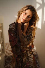 Close-up portrait of a woman in a printed robe with soft backlight. Her gentle expression and natural texture highlight quiet beauty.