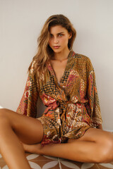 Stylish outdoor shot of a woman in a sheer lace romper posing against a tropical concrete wall. Her...