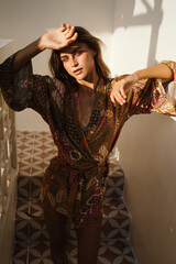 Woman in patterned kimono shielding eyes from sunlight in a relaxed pose. The golden lighting and natural setting add a cinematic feel.