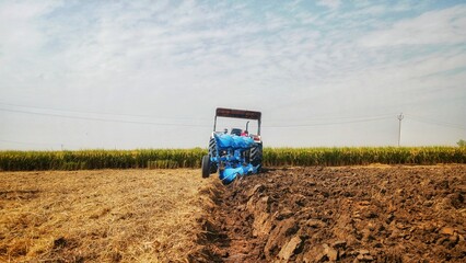 Beautiful landscape view of a tractor ploughing a field turning the golden field of rice straw into dark colour of soil creating beautiful scene during morning sky. © ANURAG GROVER
