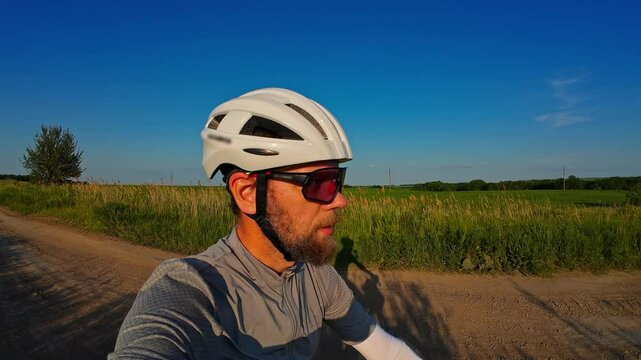 man riding bike at sunset outside city and filming video for blog, solo bike trip