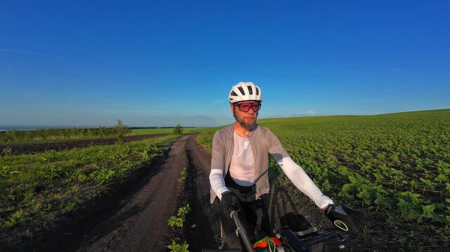 man riding bike at sunset outside city and filming video for blog, solo bike trip