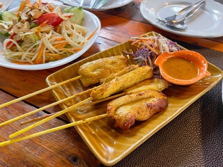 Chicken satay with peanut sauce and salad on a wooden table